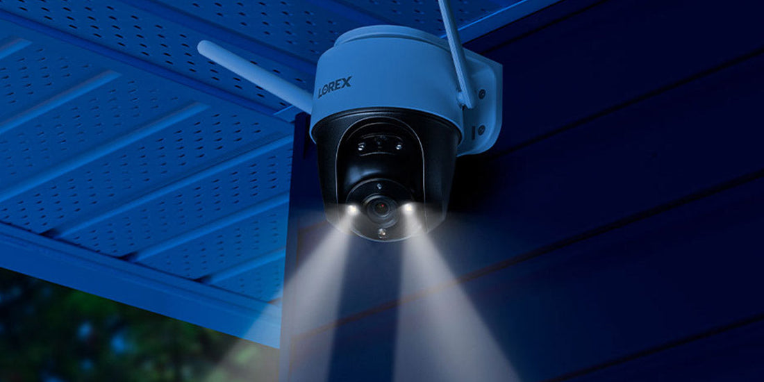 Lorex 2K pan-tilt Wi-Fi security camera mounted under an eave, with built-in dual spotlights illuminating the area at night.