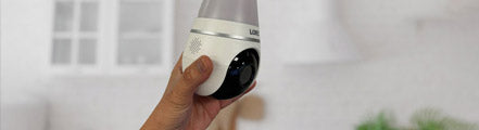  A person prepares to install a Lorex 2K Wi-Fi lightbulb security camera into an indoor ceiling socket, highlighting its simple screw-in setup and built-in camera lens.