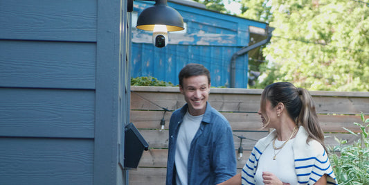  A smiling couple walks near a house entrance with a Lorex 2K Wi-Fi lightbulb security camera discreetly installed in an outdoor fixture above them.