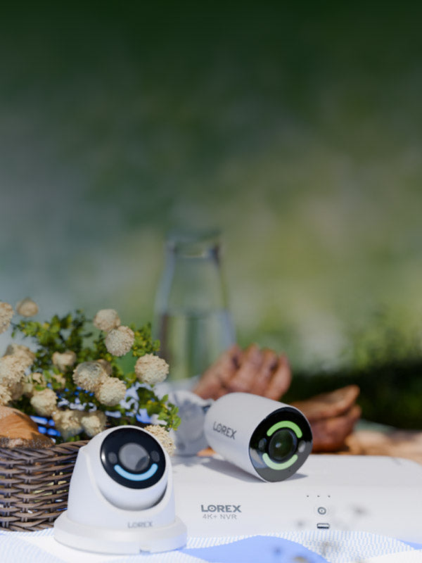 Lorex security cameras and 4K NVR on an outdoor picnic table with bread, flowers, and a spring setting in the background