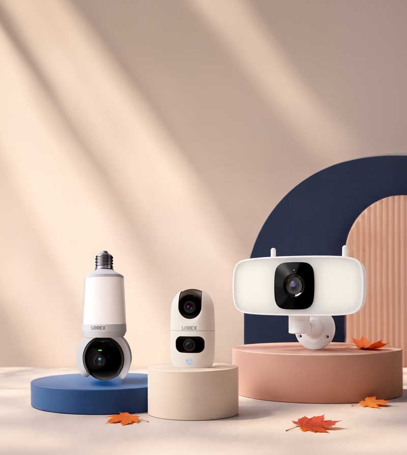 Lorex indoor Wi-Fi cameras displayed on seasonal fall-themed pedestals with autumn leaves.